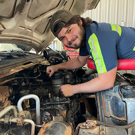 Diesel Mechanic apprentice working on truck engine and smiling at the camera